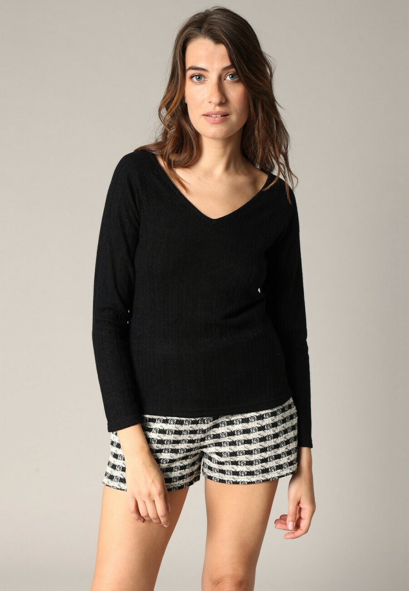Haut noir à manches longues et en V, fabriqué en tissu tricoté côtelé ; associé à un short à carreaux noir et blanc. Texture lisse, design ajusté.