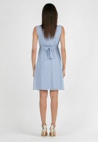Ljusblå ärmlös klänning med insvängd midja och knytning bak; faller ovanför knäet, tillsammans med guldiga högklackade skor.