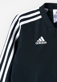 Sort Adidas-jakke med hvide tre striber på ærmerne og Adidas-logo på brystet, ribbet krave og lynlås lukning.