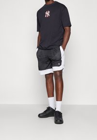 Svart kortärmad t-shirt med röd NY-logotyp, kombinerad med svarta meshshorts med vit kant och logotyp. Svarta sneakers och vita strumpor.