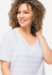 T-shirt bianco con scollatura a V, caratterizzato da strisce orizzontali testurizzate, maniche corte e una vestibilità comoda. Sono visibili capelli ricci e orecchini a cerchio.