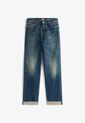 Kék farmernadrág, laza fazonnal, a térdeknél kopásnyomokkal, felhajtott szegéllyel és piros, fehér, valamint kék árnyalatú derékpánt címkével.