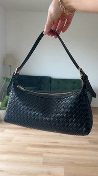 Schwarze geflochtene Lederhandtasche mit strukturierter Form, ausgestattet mit einem oberen Reißverschluss und einem langen, verstellbaren Tragegurt. Akzente aus goldfarbenem Metall.