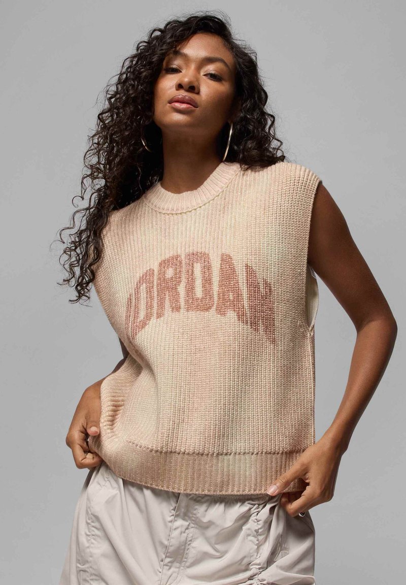 Lys beige ermeløs genser med ribbestruktur, med en fremtredende "JORDAN" logo i mørkere beige. Avslappet design med løs passform.