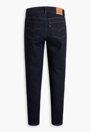 Dark blue denim jeans shown from the back with two pockets, brown stitching, a leather patch on the waistband, and a red tag on the right pocket.