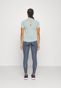 Lyseblå kortermet topp med nøkkelhullskutt bak, parret med mørkeblå leggings med perforerte mønstre og rosa detaljer.