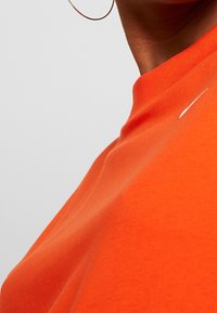 Orange kortärmad t-shirt tillverkad av mjukt bomullstyg. Har en rund hals och en liten vit logotyp vid halsringningen.