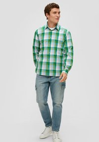 Groen en blauwe geruite shirt met lange mouwen, knoopsluiting kraag en één borstzak, gecombineerd met lichtblauwe cargo-broeken en witte sneakers.