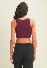 Top corto burdeos con un ajuste ceñido, tirantes gruesos y un escote redondeado, combinado con pantalones negros de cintura alta, que exhiben una textura suave.