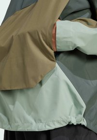 Water-resistant jacket with an olive green and mint green color block design. Features a cinched hem and sleek material with a smooth texture.