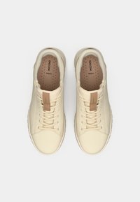 Ανοιχτά μπεζ αθλητικά παπούτσια με υφή στο επάνω μέρος, τρυπητά για αναπνοή, μπεζ κορδόνια και διακριτική δερμάτινη λεπτομέρεια στη γλώσσα.