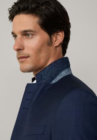 Veste marine foncé en tissu texturé, avec un col en denim contrastant et des coutures détaillées le long de l'avant et des épaules.