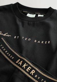Czarna bluza z okrągłym dekoltem, z logo "BAKER BY TED BAKER" w złotym kolorze na klatce piersiowej oraz pasem w złote paski.