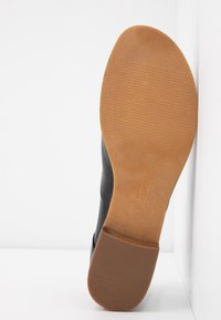 Suela de un zapato de cuero negro con suela plana de goma. La suela tiene textura con surcos, mostrando el desgaste en el dibujo y un borde liso.