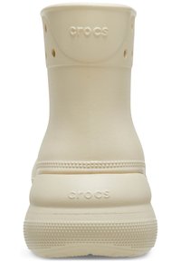 Botte Crocs beige clair avec tige texturée, trous circulaires et semelle plate à rainures. Logo à l'arrière du talon. Matériau lisse et durable.