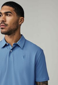 Blå polo shirt med en mjuk textur, med en klassisk krage och en liten broderad logotyp på vänster bröst. Skarp och skräddarsydd design.
