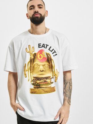 Hvit bomull T-skjorte med en gullskulptur av en burger og et ansikt, med teksten "EAT LIT!" og en rød "$6" aksent. Korte ermer, avslappet passform.