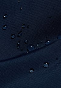 Gocce d'acqua che si aggregano su un tessuto blu scuro e texturizzato, illustrando le proprietà di repellente all'acqua o di materiale impermeabile.