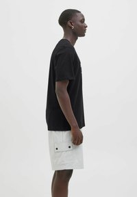 Sort bomulds t-shirt med korte ærmer, båret sammen med lysegrå cargo shorts med en sidelomme og sorte trykknapper.
