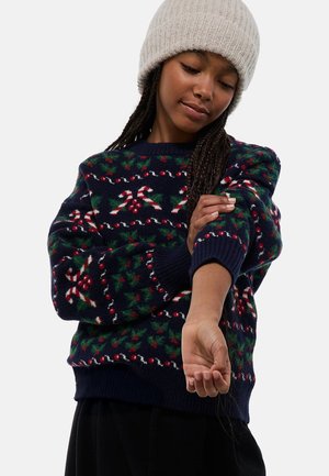 Pull en tricot bleu marine avec un motif festif de cannes de bonbon, de houx et de baies, avec des poignets et un ourlet côtelés. Tissu doux et texturé.