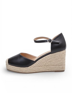 Sandalo con zeppa in pelle nera, suola piattaforma in juta intrecciata e cinturino alla caviglia con fibbia argento, vista laterale su sfondo bianco.