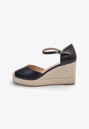 Sandalo con zeppa in pelle nera, suola piattaforma in juta intrecciata e cinturino alla caviglia con fibbia argento, vista laterale su sfondo bianco.