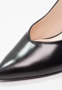 Gros plan d'une chaussure en cuir noire à bout pointu avec une tige basse et une finition lisse et brillante.