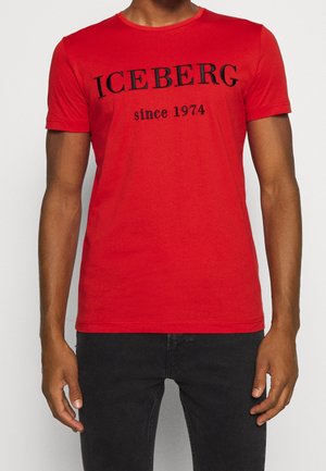 Červené bavlněné tričko s černým nápisem "ICEBERG since 1974" přes hruď, krátké rukávy a kulatý výstřih.