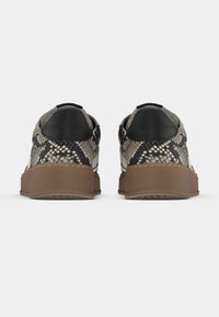 Αθλητικά παπούτσια με υφή φιδιού σε μπεζ και μαύρο, με σκοτεινή φτέρνα και καφέ λαστιχένια σόλα. Μινιμαλιστικός σχεδιασμός.