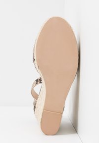 Sandale avec semelle beige, talon compensé tressé et brides à imprimé serpent, vue de dessous sur fond blanc.