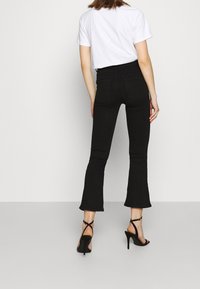 Jeans negros acampanados con cintura alta, con una textura suave y bolsillos traseros. Combinados con una camiseta blanca y tacones negros con tiras.