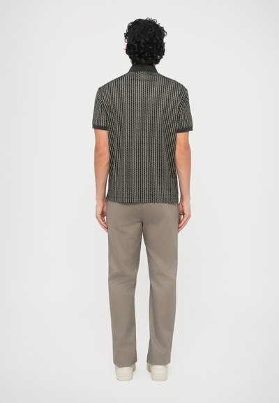 Čierna a béžová krátkym rukávom s potlačou polo košeľa s rovného strihu, kombinovaná s svetlobéžovými nohavicami a krémovými teniskami.