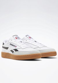 Bílé kožené tenisky s černými akcenty, gumová podrážka, šněrovací design a logo Reebok na jazyku a boku.