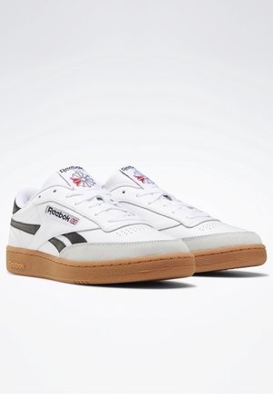 Bílé kožené tenisky s černými akcenty, gumová podrážka, šněrovací design a logo Reebok na jazyku a boku.