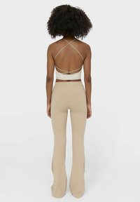 Beige geribde flared broek en een aansluitend crèmekleurig topje met kruislings straps op de rug. Gladde textuur en gestroomlijnd ontwerp.