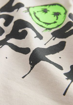 Baumwoll-T-Shirt mit einem strukturierten cremefarbenen Hintergrund, auffälligem schwarzen Graffiti-Text und einem leuchtend grünen Smiley-Gesicht.