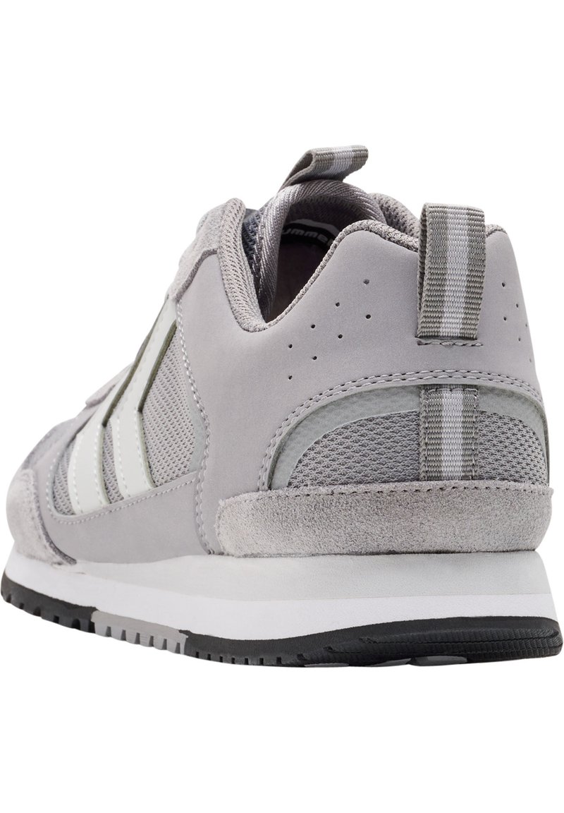 Grijze sportieve schoen met een bovenwerk van suede en mesh, witte accenten, een gestructureerde hak en een gestreepte trekband aan de achterkant. Zwarte rubberen zool.