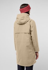 Giacca impermeabile beige con cappuccio, dotata di una apertura sul retro. Abbinata a una fascia rossa lavorata a maglia. Texture liscia, design a lunghezza intermedia.