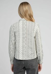 Chemise à rayures blanches et grises avec un col, un dos à boutons et une texture à motif complexe. Manches longues avec des détails aux poignets.