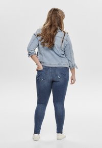 Vaaleansininen farkkutakki, jossa on käännetyt hihat, yhdistettynä tummansinisiin kapeisiin farkkuihin, joissa on takataskut ja pieniä kulumisia.