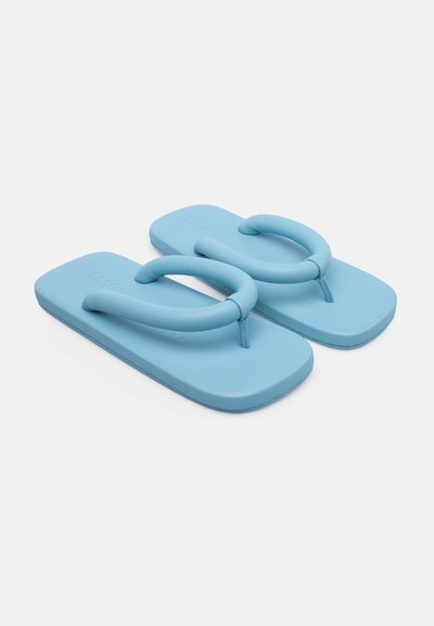 Sininen kuminen flip-flop, jossa on nilkkalenkki ja tekstuuripohja. Muotoilu on minimalistinen, sileällä pinnalla ja tasaisella pohjalla.