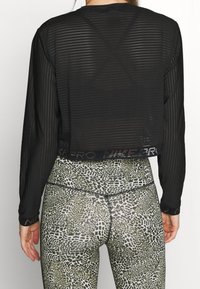 Top nero a maniche lunghe cropped con righe orizzontali e tessuto trasparente, abbinato a leggings a vita alta con stampa leopardata verde.