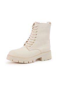 Jasnobeżowy bojowy but z okrągłym noskiem, przednią częścią na sznurowadła oraz grubą gumową podeszwą z fakturą. Gładki syntetyczny materiał.