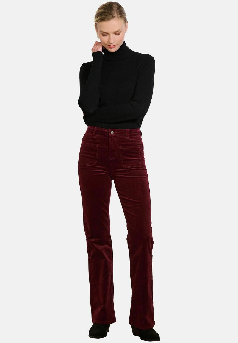 Pantalones acampanados de pana burdeos con bolsillos frontales y cierre de botón, combinados con un suéter negro ajustado de cuello alto.