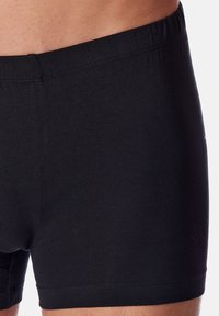 Boxers en coton noir avec une taille élastique, présentant une texture lisse et un design ajusté, avec des coutures visibles le long des bords.