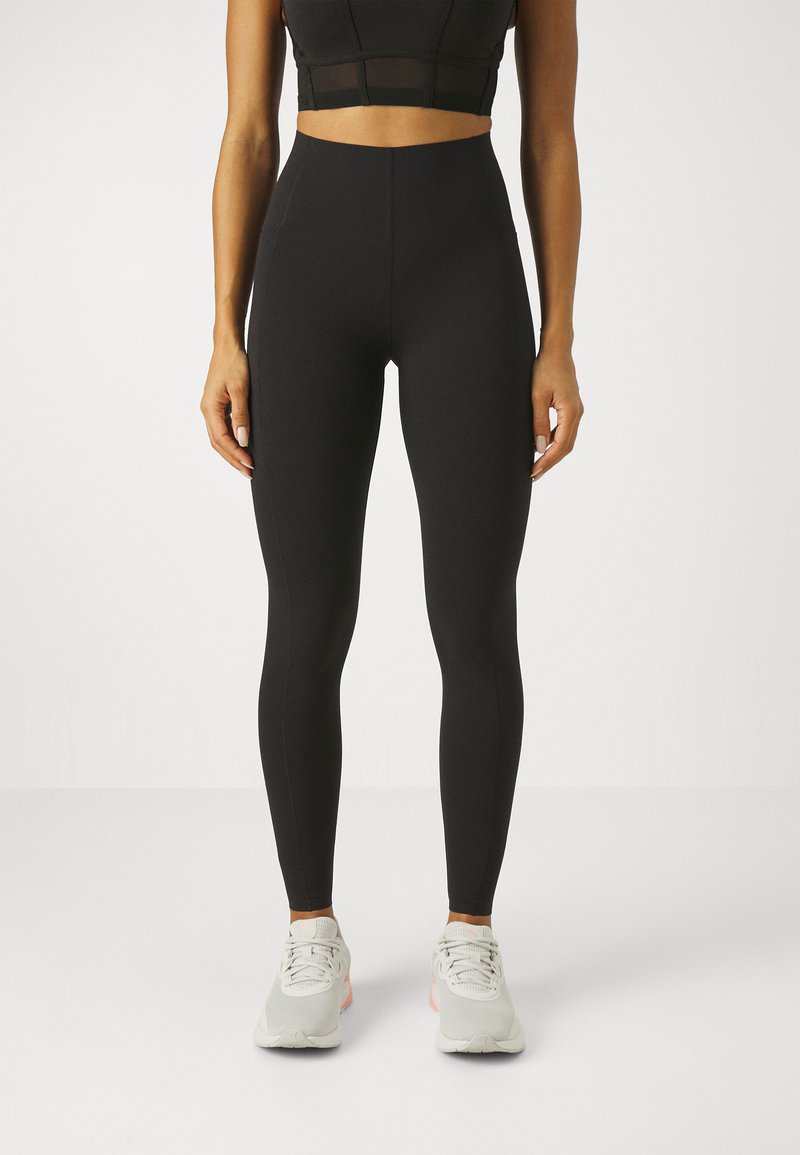 Høyt liv svarte leggings laget av elastisk materiale, med en jevn tekstur og en figurnær design, sammen med grå og rosa joggesko.