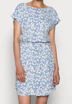 Woman wearing a short-sleeve, knee-length blue dress with white floral pattern and drawstring waist against a plain background.
