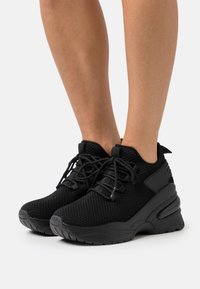 Chaussures de sport noires en mesh, avec une semelle épaisse, un bout arrondi et des lacets tissés. Des accents lisses sur les côtés améliorent le design.