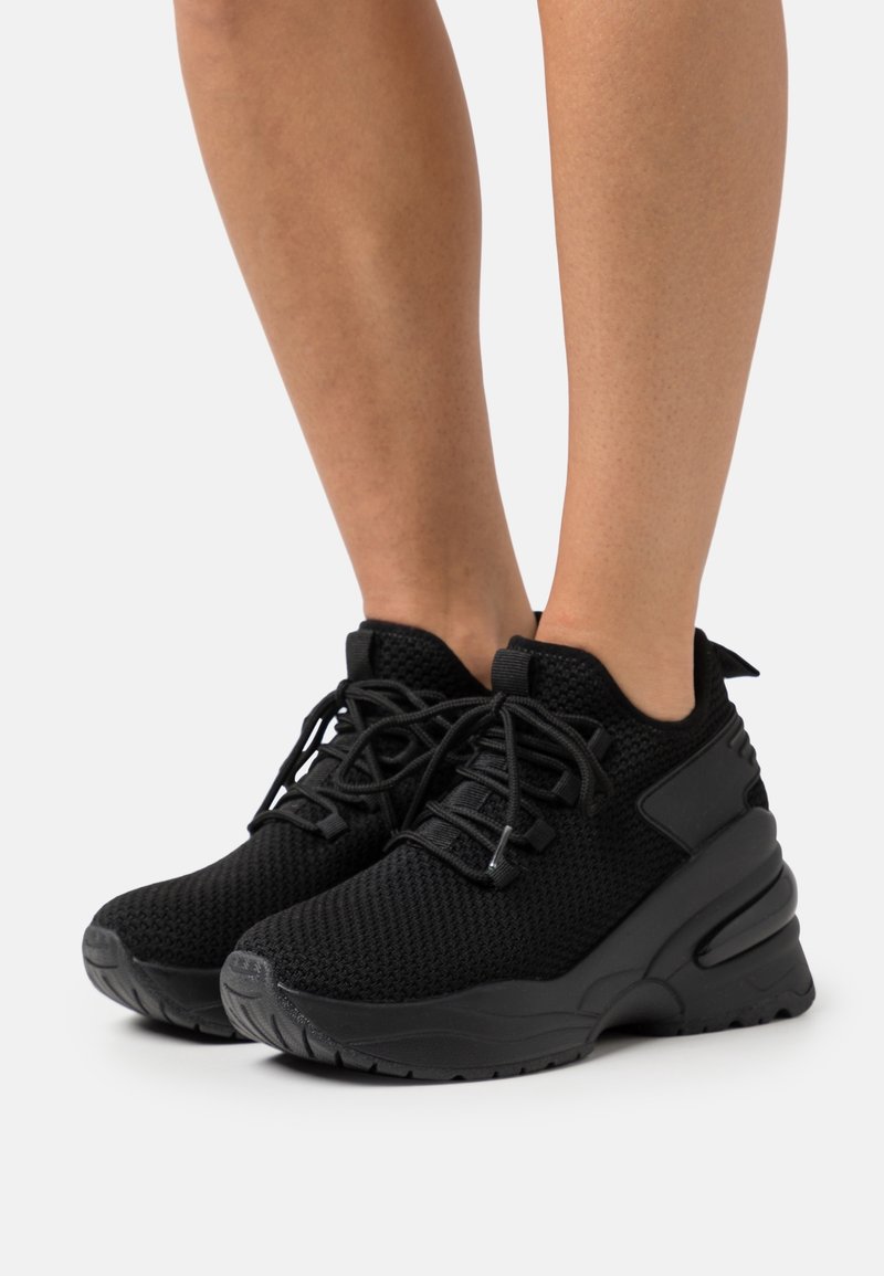 Chaussures de sport noires en mesh, avec une semelle épaisse, un bout arrondi et des lacets tissés. Des accents lisses sur les côtés améliorent le design.