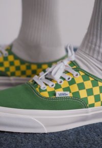 Green and yellow checkered Vans sneakers with white laces and rubber soles, featuring a canvas upper and a Vans logo on the side.